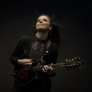 a dark-toned photo of a smiling young white woman playing a mandolin